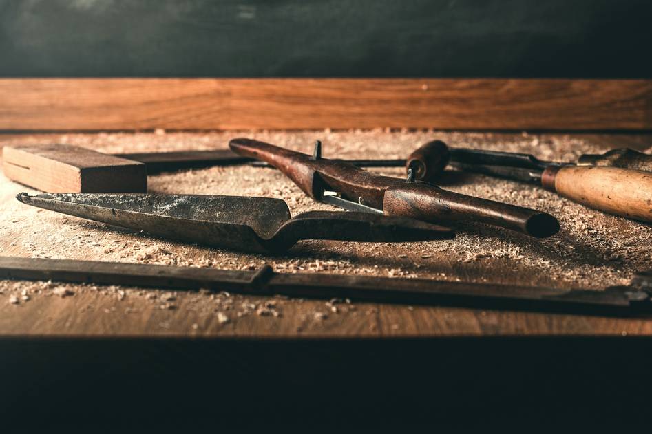 Hand operating a scroll saw with fine wood dust and detailed cutout pieces nearby